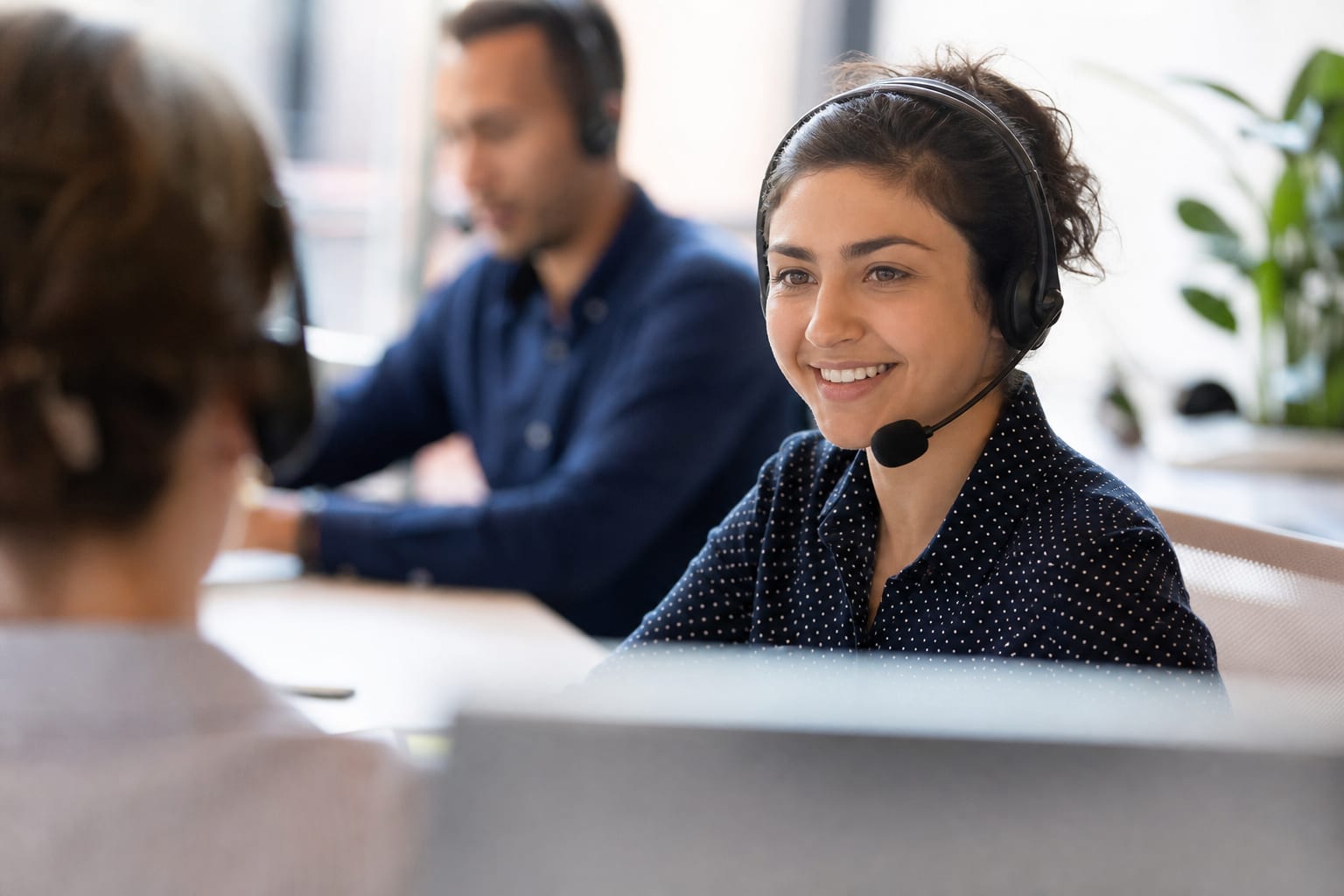 Agen customer service dengan headset berbicara kepada pelanggan di layar komputer, keduanya tersenyum