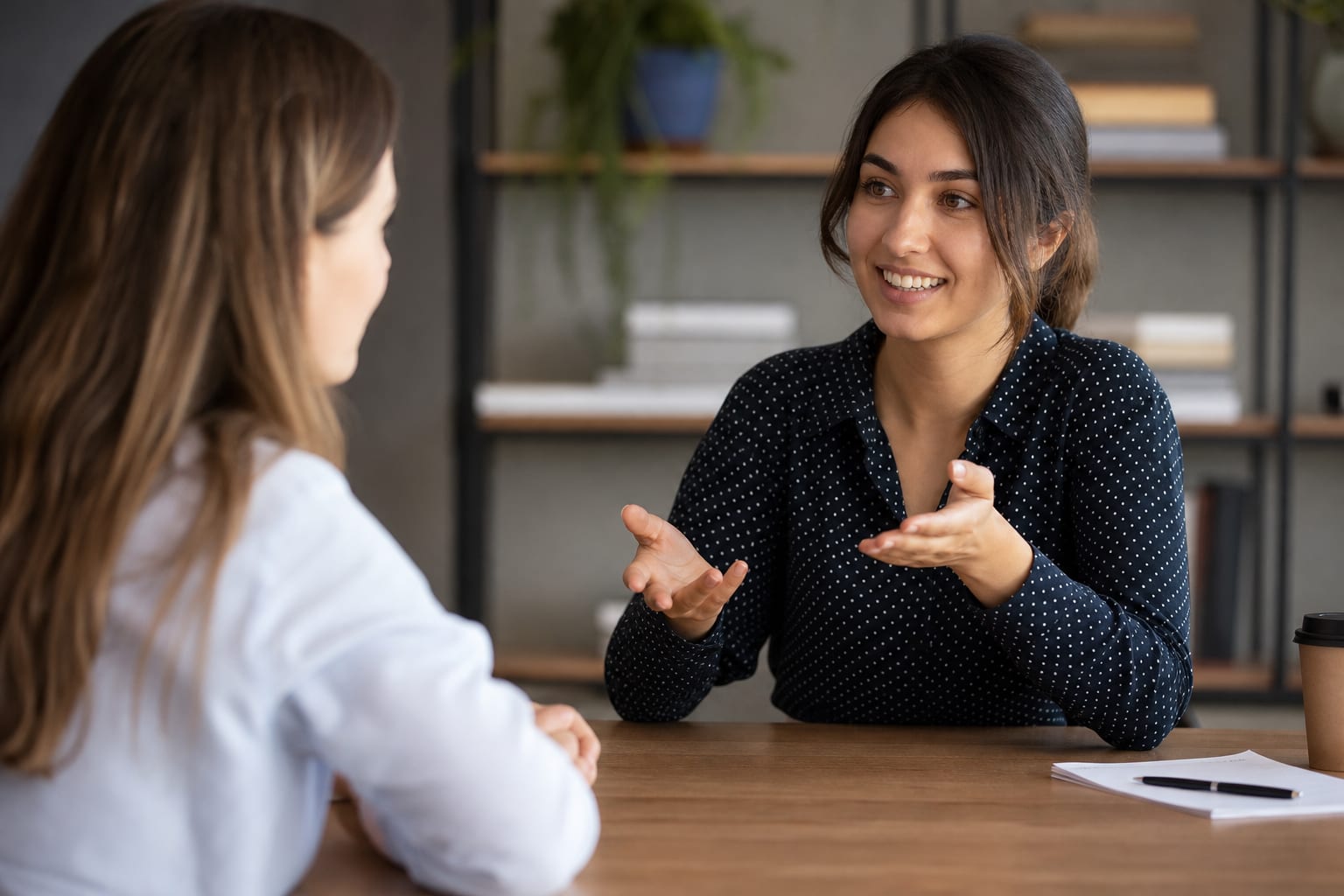 Two students sitting at a small table facing an examiner, one pointing at a photograph while speaking