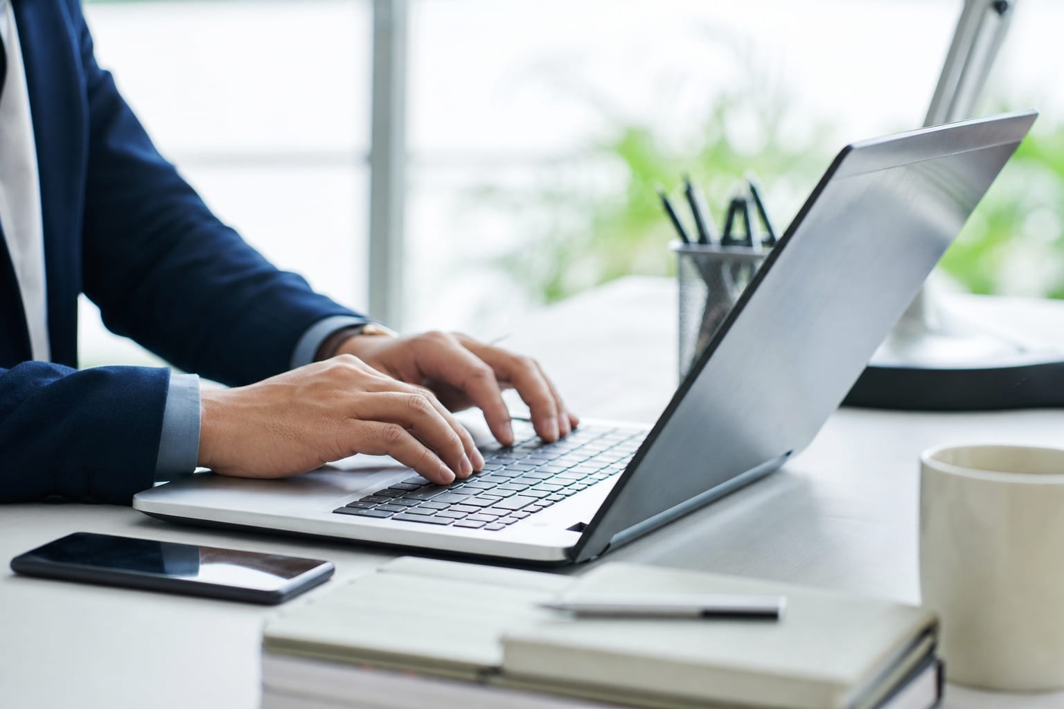En pult med en laptop som viser et e-postutkast, et notatblokk med håndskrevne fraser og en kaffekopp ved siden av